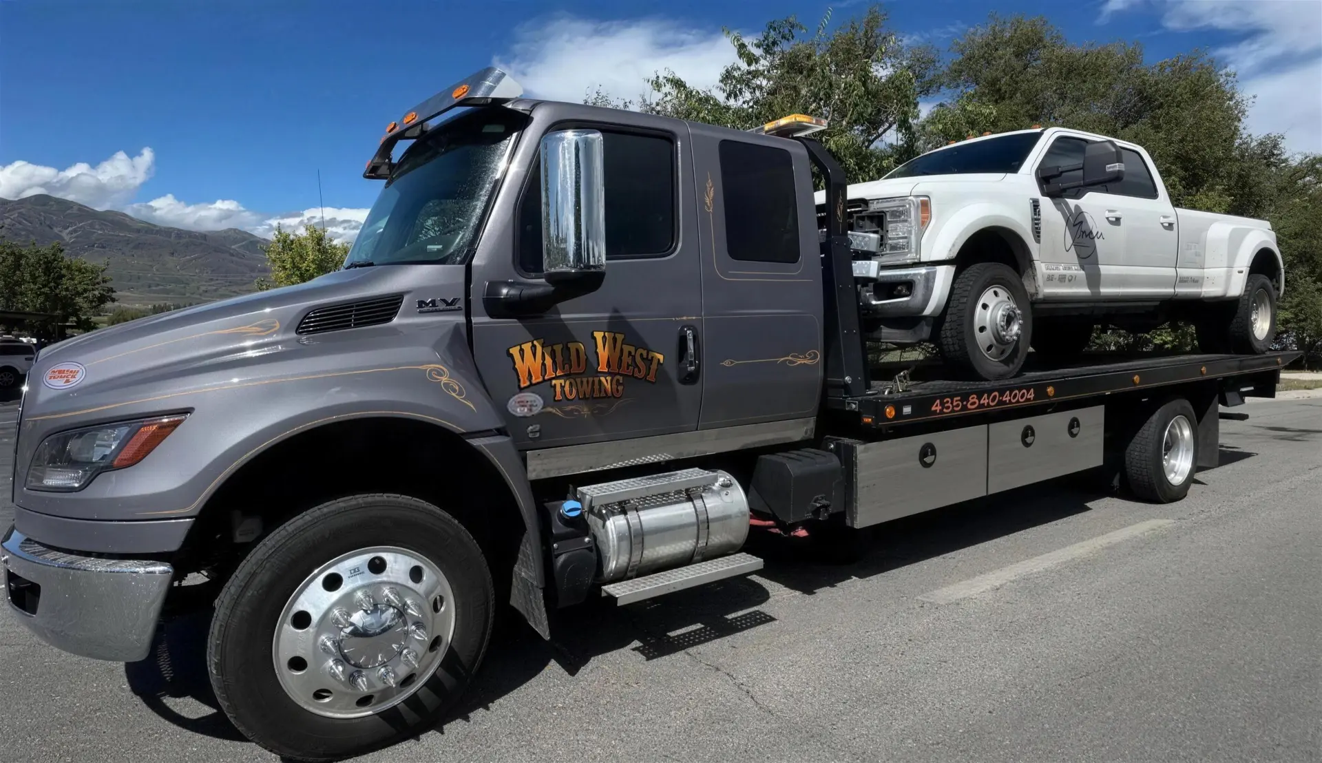Wild West Towing flatbed hauling a white Ford dually pickup with the mountains behind it